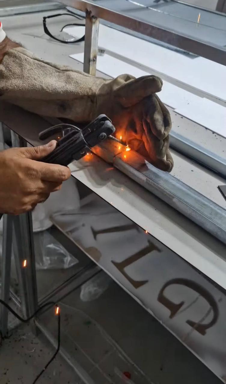 Profissional realizando soldagem em estrutura metálica durante produção de comunicação visual