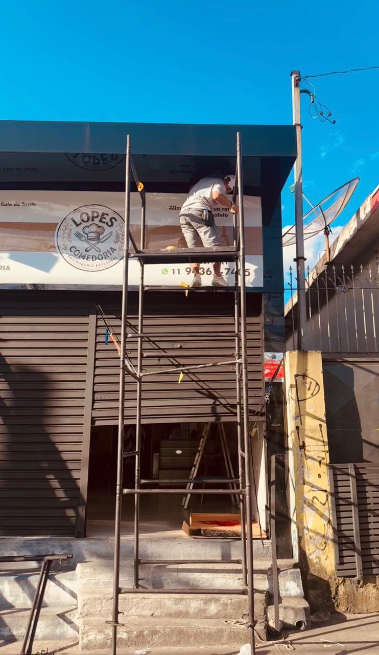 Profissional realizando instalação de comunicação visual em fachada comercial